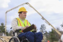 Construction supervisor with Spinal Cord Injury taking notes with concrete pump in background — Stock Photo