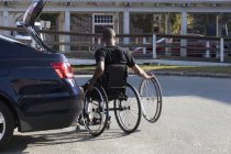 Человек, у которого был менингит позвоночника в инвалидной коляске, садится в свою машину — стоковое фото