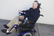 Людина з травмами спинного мозку і рука з нервовими пошкодженнями в моторизованому інвалідному візку, дивлячись на смартфон — стокове фото