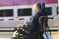 Homem com lesão medular usando sua cadeira de rodas motorizada à espera de trem público — Fotografia de Stock