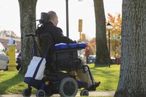 Человек с травмой спинного мозга и руки с повреждением нерва в моторизованной инвалидной коляске в общественном парке — стоковое фото
