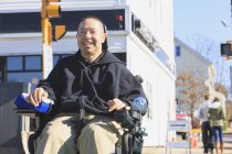 Людина з травмами спинного мозку і рука з нервовими пошкодженнями в моторизованому інвалідному візку, що перетинає громадську вулицю під час покупок — стокове фото