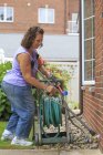 Frau mit Spina bifida mit Krücken und Gartenschlauch ziehen — Stockfoto