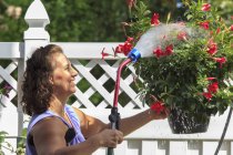 Frau mit Spina bifida versprüht Blumen mit Gartenschlauch — Stockfoto