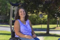 Femme avec Spina Bifida rire tout en étant assis en fauteuil roulant avec des béquilles — Photo de stock