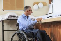 Інженер проекту з травмою спинного мозку в інвалідному візку, який дивиться на малюнки — стокове фото
