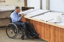 Ingegnere di progetto con una lesione del midollo spinale su una sedia a rotelle utilizzando un tablet per studiare disegni — Foto stock