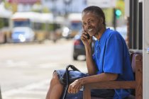 Hombre con lesión cerebral traumática esperando en la terminal de autobuses mientras está en su teléfono - foto de stock