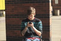 Hombre de moda con una lesión en la médula espinal en silla de ruedas tomando sus mensajes de texto - foto de stock