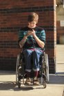 Модний чоловік з травмою спинного мозку в інвалідному візку приймає текстові повідомлення — стокове фото