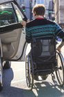 Модный человек с травмой спинного мозга в инвалидном кресле садится в такси — стоковое фото