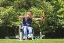 Man with spinal cord injury in wheelchair aiming his bow and arrow for archery practice — Stock Photo