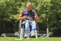 Uomo con lesione del midollo spinale in sedia a rotelle preparazione per la pratica di tiro con l'arco — Foto stock