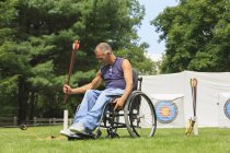 Человек с травмой спинного мозга в инвалидной коляске готовится к практике стрельбы из лука — стоковое фото