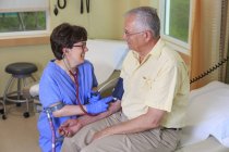 Krankenschwester mit Zerebralparese bei der Blutdruckmessung eines Patienten in einer Klinik — Stockfoto