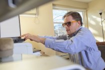 Man with congenital blindness scanning paperwork at his computer — Stock Photo