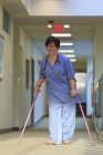 Infirmière avec paralysie cérébrale marchant dans le couloir d'une clinique avec ses cannes — Photo de stock