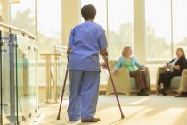 Enfermeira com Paralisia Cerebral caminhando pelo corredor de uma clínica com seus bastões — Fotografia de Stock