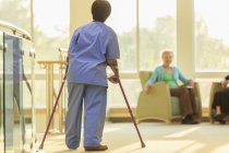 Enfermeira com Paralisia Cerebral caminhando pelo corredor de uma clínica com seus bastões — Fotografia de Stock