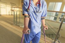 Enfermera con parálisis cerebral caminando por el pasillo de una clínica con sus bastones - foto de stock