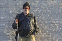 Uomo con cecità congenita in piedi davanti a un muro con il bastone — Foto stock