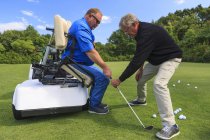 Homem com lesão medular em um carrinho adaptativo no golfe colocando verde com um instrutor — Fotografia de Stock