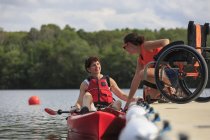 Instructor que ayuda a una mujer con una lesión en la médula espinal a usar un kayak - foto de stock