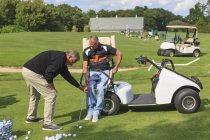 Человек с травмой спинного мозга в адаптивной тележке в гольф положить зеленый с инструктором — стоковое фото