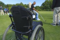 Mann mit Querschnittslähmung in einem adaptiven Cart auf dem Golf Putting Green mit einem Trainer — Stockfoto
