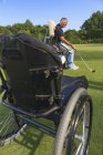 Человек с травмой спинного мозга в адаптивной тележке в гольф положить зеленый — стоковое фото