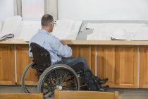 Інженер-проектувальник з травмою спинного мозку в інвалідному візку, який працює над кресленнями — стокове фото