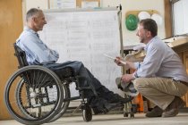 Два інженери проекту використовують підвісну стійку для планів робочих місць, один у інвалідному візку з травмою спинного мозку — стокове фото