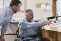Два инженера проекта используют планшет, чтобы проверить планы работы, один в инвалидном кресле с травмой спинного мозга — стоковое фото