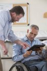 Dos ingenieros de proyecto que utilizan su tableta para comprobar los planes del lugar de trabajo, uno en una silla de ruedas con una lesión en la médula espinal - foto de stock
