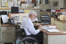 Чоловік з м'язовою дистрофією в інвалідному візку пише в своєму офісі — стокове фото