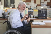 Человек с мышечной дистрофией в инвалидном кресле с планшетом за рабочим столом — стоковое фото