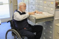 Uomo con distrofia muscolare in sedia a rotelle utilizzando un sistema di archiviazione nel suo ufficio — Foto stock