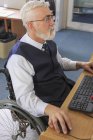 Uomo con distrofia muscolare su una sedia a rotelle che lavora al suo computer in un ufficio — Foto stock