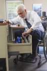 Homme atteint de dystrophie musculaire dans un fauteuil roulant prenant des dossiers d'information de son tiroir de bureau — Photo de stock