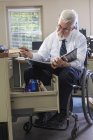 Чоловік з м'язистою дистрофією в інвалідному візку дивиться на файл зі свого настільного ящика — стокове фото