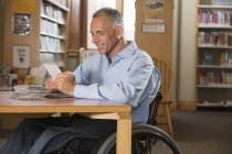 Homme en fauteuil roulant avec une blessure à la moelle épinière dans une bibliothèque regardant des DVD — Photo de stock