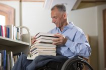 Uomo in sedia a rotelle con lesione al midollo spinale che sceglie libri da uno scaffale di una biblioteca — Foto stock