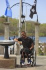 Man in a wheelchair who had Spinal Meningitis at a park with a water fountain — Stock Photo