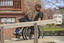 Homem em uma cadeira de rodas que tinha meningite espinhal usando uma rampa de construção pública — Fotografia de Stock