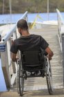 Homem em uma cadeira de rodas que tinha meningite espinhal descendo uma rampa para uma doca — Fotografia de Stock