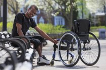 Hombre que tenía meningitis espinal sentado en un banco del parque cerca de su silla de ruedas - foto de stock