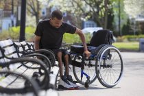 Homem que teve meningite espinhal saindo de um banco de parque e em sua cadeira de rodas — Fotografia de Stock