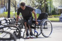Hombre que tenía meningitis espinal saliendo de un banco del parque y en su silla de ruedas - foto de stock