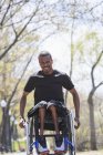Man in a wheelchair who had Spinal Meningitis going through a park — Stock Photo