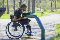 Homme en fauteuil roulant atteint de méningite rachidienne utilisant une fontaine d'eau publique — Photo de stock